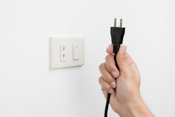 Hand of man unplug electric outlet plug on wall white background safety concept