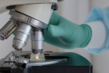 Close up view of scientist hands with gloves set the sample in the microscope for research