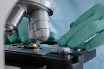 Close up view of scientist hands with gloves set the sample in the microscope for research