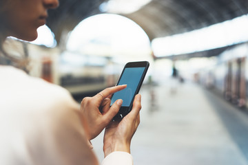 Enjoying travel. Young pretty woman waiting on the station platform with backpack on background electric train using smartphone. Tourist texting message and plan route of railway, railroad concept