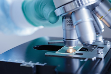 Close up view of scientist hands with gloves set the sample in the microscope for research