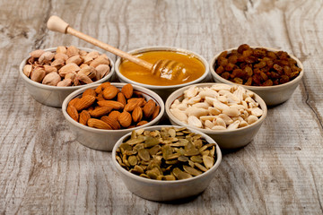 Pistachios, almonds, peanuts, pumpkin seeds, raisins and honey in ceramic plates.