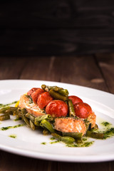 Grilled trout with tomatos leguminous beans and lemon on white plate. Top view wooden back ground