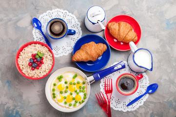 Traditional breakfast with eggs, oatmeal porridge, croissants and coffee on grey background with copy space. Top view