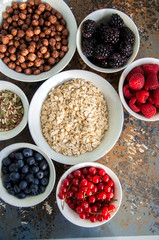 Oat, raspberries, red currant, blueberries, blackberries, chocolate balls in bowls on a rusty background