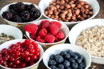 Oat, raspberries, red currant, blueberries, blackberries, chocolate balls in bowls on a rusty background