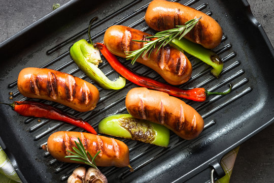 Fried sausages with  vegetables in grill pan at black background