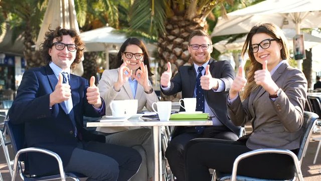 Happy businesspeople showing thumbs to the camera in the cafe
