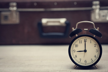 retro style image of alarm clock showing nine with vintage suitcase on the background. closeup.