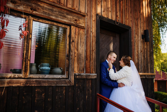 Wedding couple against old wooden house with red leaves on his.