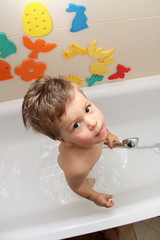 Small boy standing in the white bath with shower in hand