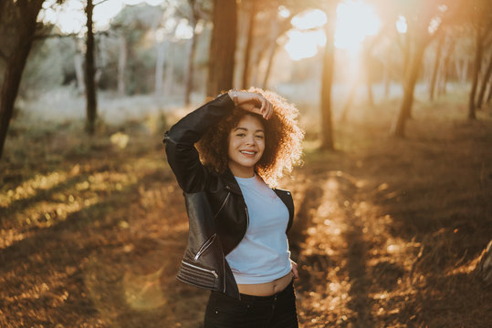 Chica paseando por el bosque feliz y con el atardecer detr&aacute;s