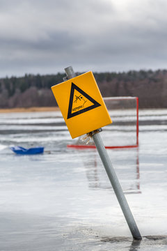 Yellow warning sign and hockey goal on wet melting ice on frozen lake, Sweden. 