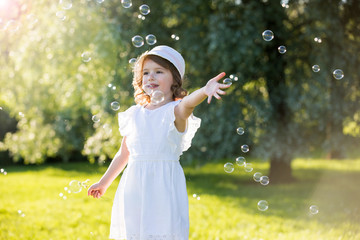 Adorable little girl, has happy fun with cheerful smiling face. Carefree child laughing, Running and jumping on green summer meadow, catching soap bubbles. Happiness, childhood and freedom concept.