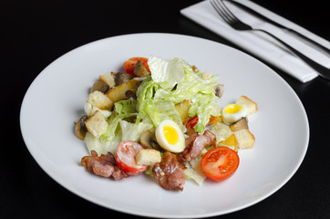 Salad with fried bacon and vegetables on a white plate on a black background