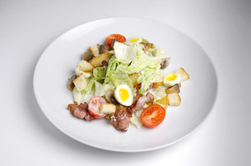 Salad with fried bacon and vegetables on a white plate on a white background