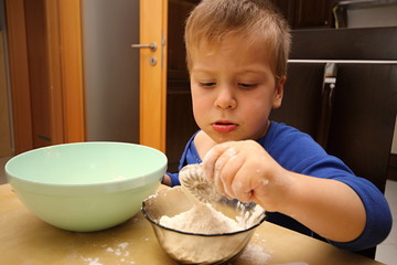 Boy cooking sweets with flour and saucer holding shape