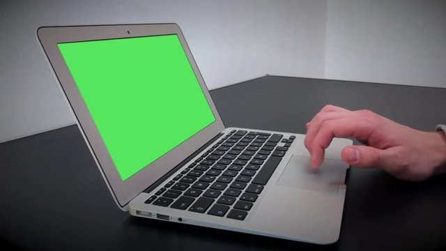 Man's hand using and scrolls track pad laptop. Computer, notebook with chromakey on a black table in a room with white walls. 4k video.
