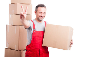 Smiling mover man holding cardboard box and showing peace