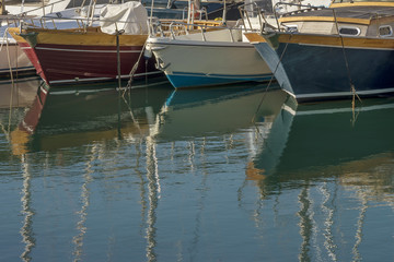 Fototapeta na wymiar Bows of beautiful boats anchored in the marina of Talamone, Grosseto, Tuscany, Italy, create wonderful reflections on the water of the freshly choppy sea