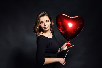 Obraz na płótnie Canvas Beautiful girl holding a big red balloon in the form of hearts,Valentine's Day.Red hearts close up,Beauty portrait of female face with make up,sexy gloss lips make-up and dark eyebrows,makeup concept