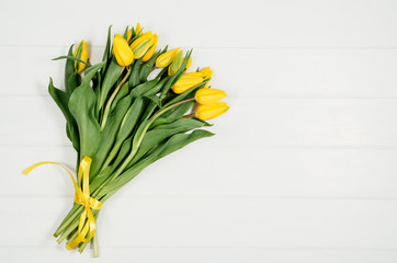 Background with yellow tulips on white wooden table top view. Creative woman's workspace concept with copy space. Product photograph taken from above with frame composition