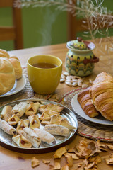 Black tea in yellow mug with croissants, buns and homemade cookies on wooden table