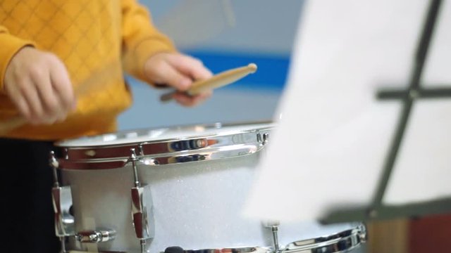 Teen musician playing drum reading sheet music during school fair. Focus on the drum