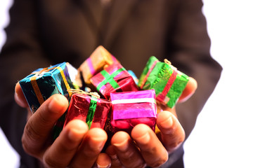 Man in a black suit holds Christmas gifts wrapped in a box with ribbon and bow isolated on a white background