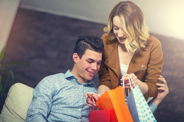 Young couple is sitting at sofa at home and looking at shopping bags