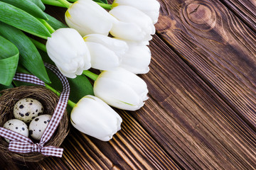 Bouquet white  tulip flowers with easter eggs on old wooden table. Place for text.
