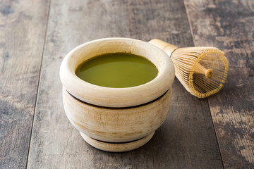Matcha green tea in a bowl and bamboo whisk, on wooden background
