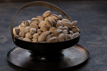 Pistachio in metal bowl. Dark photography. Dark grey wooden background.