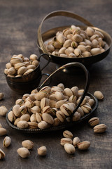 Pistachio in metal bowl. Dark photography. Dark grey wooden background.