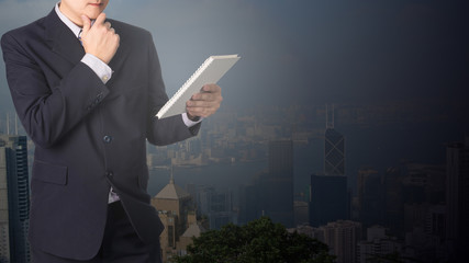 Double exposure Confident Asian businessman reading notebook or document file with cityscape on blurred building.