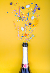 Colorful party attributes fly out from botle of champagne wine. on a yellow background. Flat lie. Celebrate concept. High resolution photo. - obrazy, fototapety, plakaty