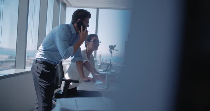 Businessman talking on mobile phone while businesswoman using computer in office. Business people working together in office.