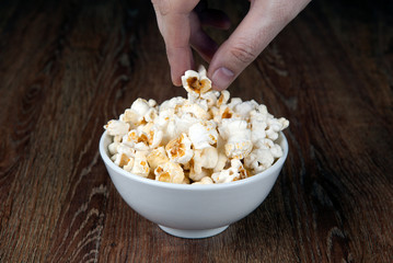 bowl filled with salt popcorn on a wooden table and human hand