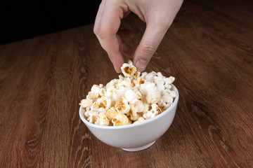 bowl filled with salt popcorn on a wooden table and human hand