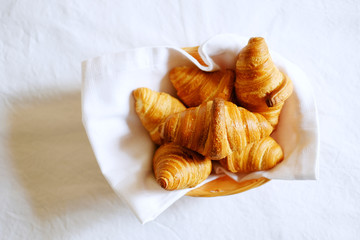 Croissants in woven basket with white napkin on linen bedding