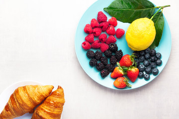 mixed berries and croissants on a blue plate on a white background