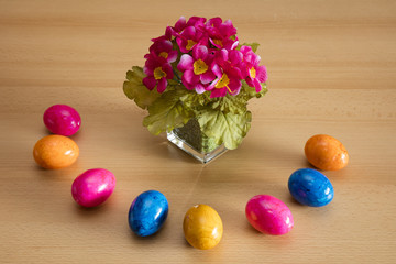 Vase mit künstlichen Primeln und farbige Ostereier