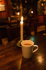 Cup of coffee and candle stands on a table in a dark room cafe. Copy Space, vertical photo.