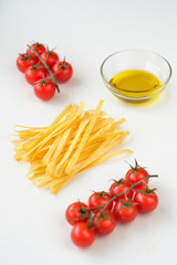 Uncooked italian pasta, olive oil and tomatoes cherry on a white background