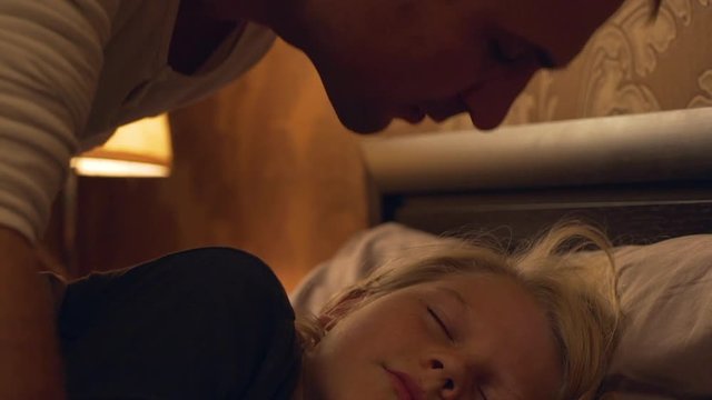 Close up footage of blonde young child sleepin in bed while his middle-aged kissing him in slowmotion