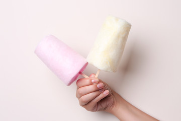 Female hand holding sweet cotton candies on color background