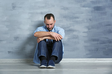 Handsome depressed man sitting on floor near wall