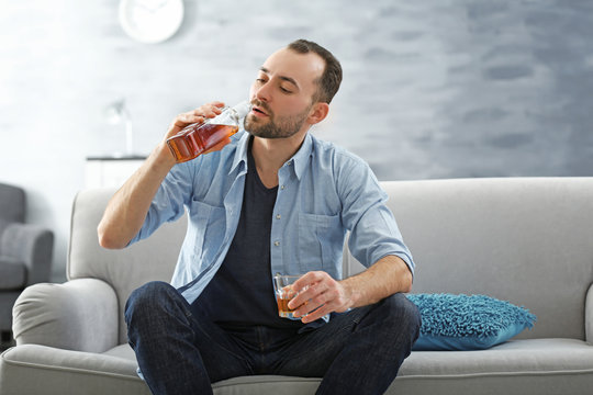 Handsome depressed man drinking whisky at home