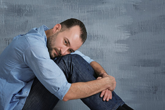 Handsome depressed man sitting near wall at home