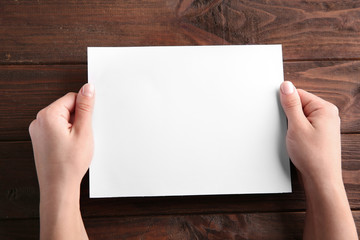 Obraz premium Female hands holding empty paper sheet on wooden background
